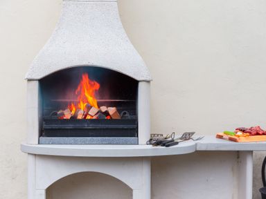 An outdoor fireplace with fire burning beside grill tools at Carines Barns - Wesley Barn, Cubert