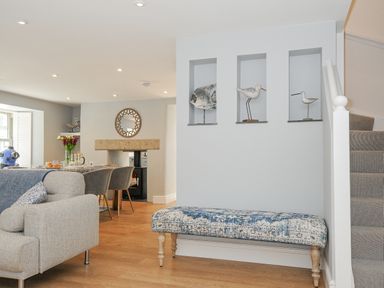 A living area with a bench under cubbyholes containing bird sculptures by stairs at Cob Cottage near Rock
