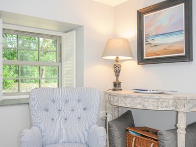 A corner of a room with a striped armchair a decorative table with a lamp and a painting near Cob Cottage near Rock
