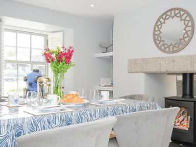 A dining area with a table set with plates cups and croissants near a window and a fireplace at Cob Cottage near Rock