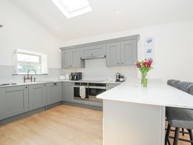 A kitchen with grey cabinets a white marble countertop flowers on the island and wooden floor at Cob Cottage near Rock