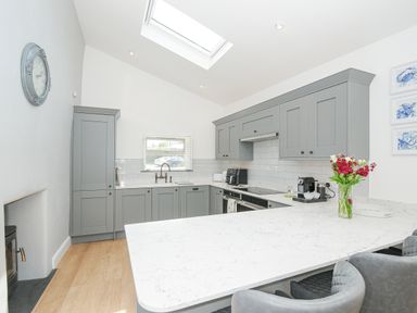 A kitchen with gray cabinets a white marble countertop a skylight and a vase of flowers at Cob Cottage near Rock