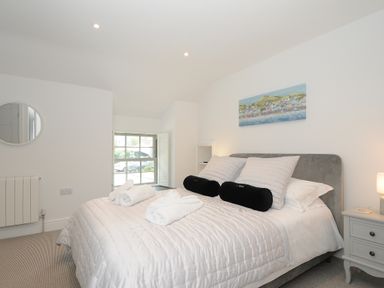 A bedroom with a bed with white bedding and black pillows a window and a bedside table at Cob Cottage near Rock