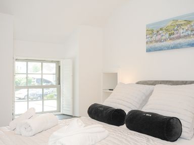 A bedroom with a bed with white pillows and black bolsters near a window at Cob Cottage near Rock