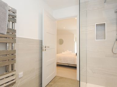 A bathroom with a heated towel rail and a shower opening into a bedroom with a bed and round mirror at Cob Cottage near Rock