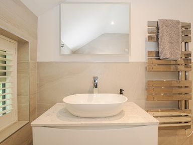 A bathroom vanity with an oval sink a mirror above and a towel rack with a towel at Cob Cottage near Rock