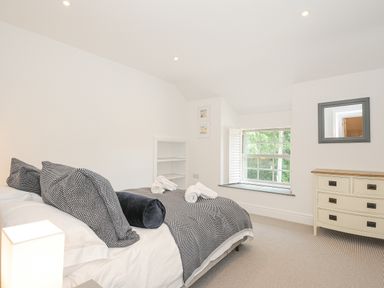 A bedroom with a bed with pillows and blankets a dresser a window and a mirror at Cob Cottage near Rock