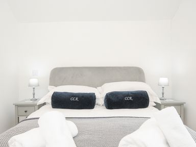 A bedroom with a double bed two bedside tables with lamps and folded towels at Cob Cottage near Rock
