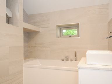 A bathroom with a bathtub a rectangular sink and a small window at Cob Cottage near Rock