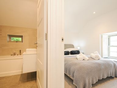 A bedroom with a bed and rolled towels and an adjacent bathroom with a bathtub near Cob Cottage near Rock