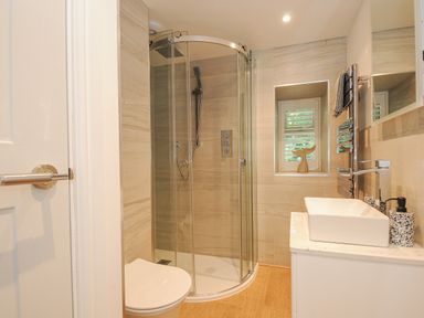 A bathroom with a glass shower enclosure a toilet a sink with a faucet and a small window at Cob Cottage near Rock