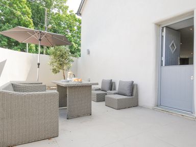 An outdoor patio with gray wicker chairs a table with breakfast items and a large umbrella at Cob Cottage near Rock