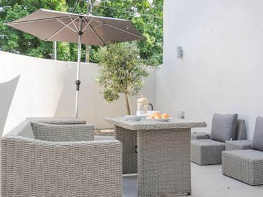 An outdoor patio area with wicker furniture a table with plates croissants and a coffee press under a large umbrella at Cob Cottage near Rock