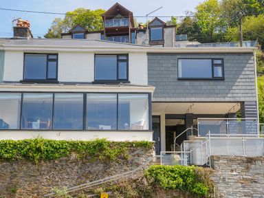 The exterior of a two-story house with large windows and a stone retaining wall at Anjoma in Looe