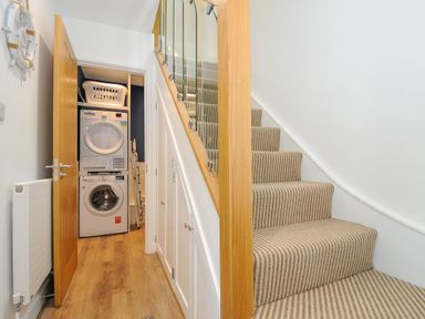 A hallway with a staircase and a laundry area with stacked washer and dryer at Anjoma in Looe