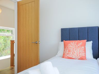 A bedroom with a bed with blue headboard and coral pillow with white design near a wooden door at Anjoma in Looe