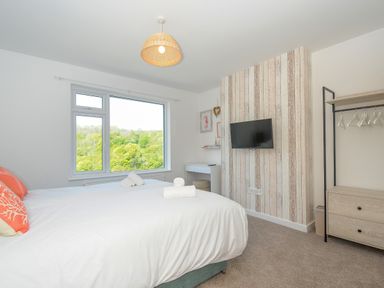 A bedroom with two beds near a large window a wall-mounted tv and an open wardrobe at Anjoma in Looe