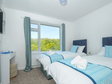 A bedroom with two single beds and a window showing a green landscape at Anjoma in Looe