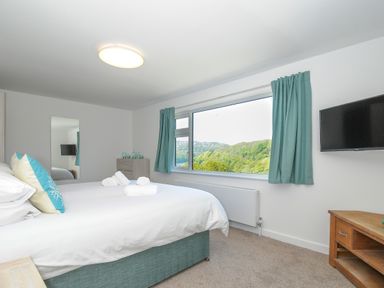 A bedroom with a large bed pillows rolled towels on the bed window with green curtains and a wall mounted television at Anjoma in Looe