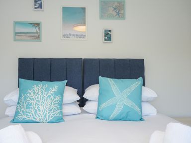 A bed with blue headboards and two blue pillows with sea designs and framed pictures on the wall at Anjoma in Looe