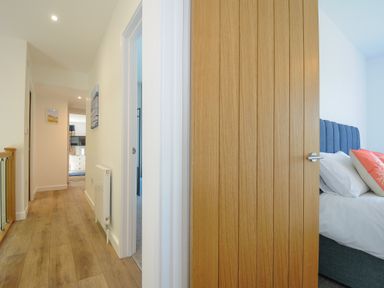 A hallway with wooden flooring and doors leading to bedrooms at Anjoma in Looe