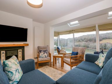 A living room with blue sofas wooden chairs and a television mounted above a fireplace at Anjoma in Looe