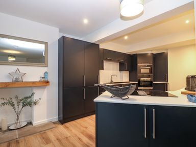 A kitchen with black cabinets wooden floor and countertop with decorative items at Anjoma in Looe