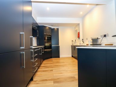 A kitchen with dark cabinets white countertops wooden floor and built in appliances at Anjoma in Looe