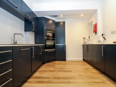A kitchen with dark cabinets, built-in oven, white countertops, wooden floor, and appliances on the counter at Anjoma in Looe