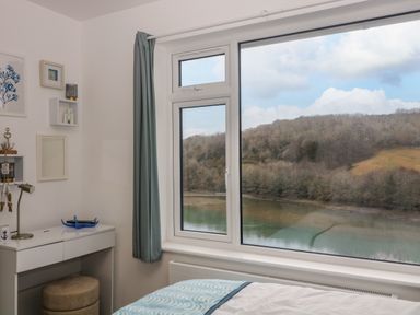 A bedroom with a window showing a river and wooded hills at Anjoma in Looe