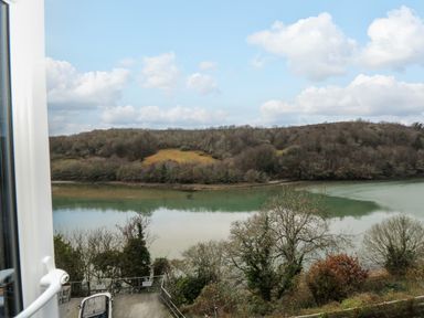 A view through a window of a river with trees on the bank and hills in the background at Anjoma in Looe
