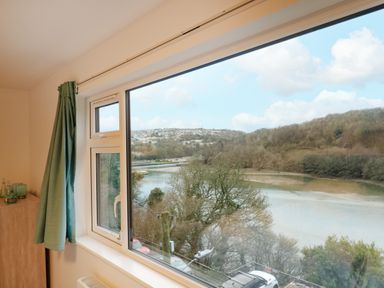 A window with green curtains overlooking a river and trees at Anjoma in Looe