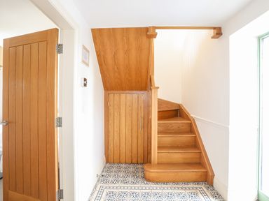 A hallway with wooden stairs and a wooden door under the stairs a tiled floor at Gwalia Cottage in Brynsiencyn