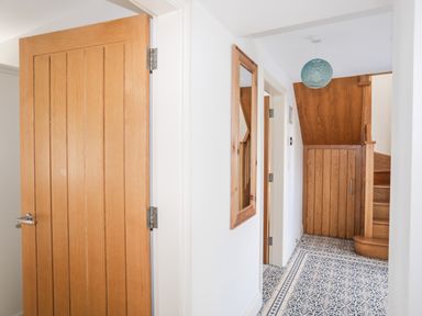 A hallway with a wooden door, mirror on the wall, patterned tile floor, wooden staircase, and blue hanging light at Gwalia Cottage in Brynsiencyn