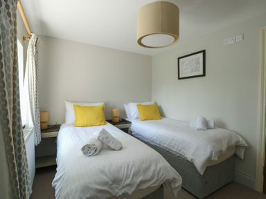 A bedroom with two single beds with yellow pillows and rolled towels at Gwalia Cottage in Brynsiencyn