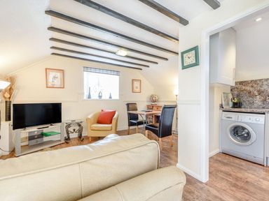 A living room with a television armchairs dining table and an adjacent kitchen at The Hayloft in St Florence