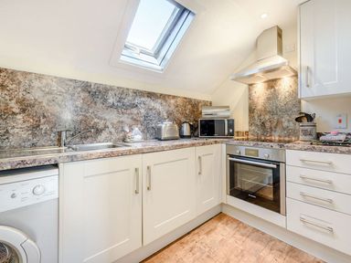 A kitchen with white cabinets granite countertops a skylight microwave oven and washing machine at The Hayloft in St Florence