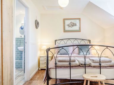 A bedroom with a metal bed frame bedside tables with lamps folded towels on the bed and a view into a bathroom at The Hayloft in St Florence