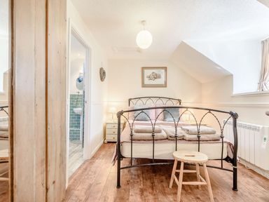A bedroom with a metal framed bed wooden stool bedside tables with lamps and an ensuite bathroom at The Hayloft in St Florence