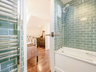 A bathroom with a bathtub shower and green tiled walls next to a bedroom with a bed and dresser at The Hayloft in St Florence