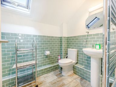 A bathroom with a toilet sink towel rack and green tiled walls at The Hayloft in St Florence