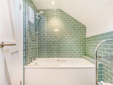 A bathroom with a bathtub shower and green tiled walls at The Hayloft in St Florence