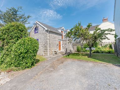 A stone building with purple window frames and orange doors beside a gravel driveway and green trees at The Hayloft in St Florence