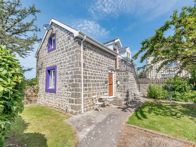 Stone house with purple window frames and white chairs and tables outside in garden at The Hayloft in St Florence