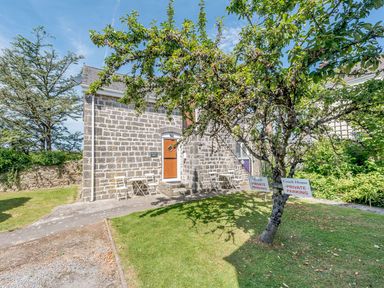 A stone building with wooden doors and white chairs outside under a tree with private parking signs at The Hayloft in St Florence