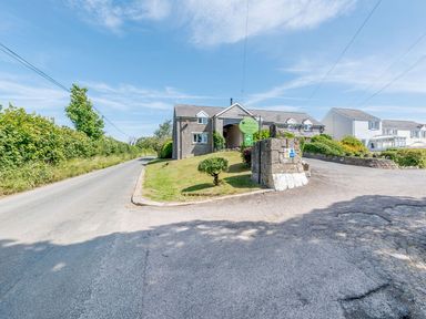 A stone building with a green sign on a grassy area beside a road at The Hayloft in St Florence