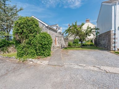 A gravel parking area with a stone building and a small garden with trees at The Hayloft in St Florence