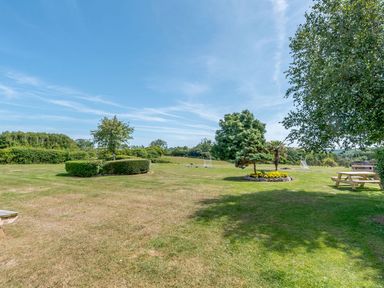 An open grassy garden area with trees bushes and wooden picnic benches at The Hayloft in St Florence