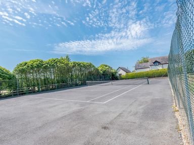 An outdoor tennis court with a net a house and trees in the background at The Hayloft in St Florence