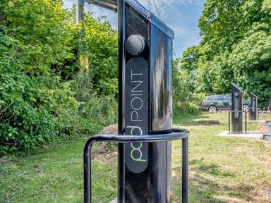 Electric vehicle charging stations in a grassy outdoor area with trees and a parked car at The Hayloft in St Florence